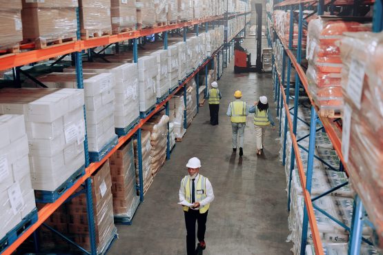 Warehouse, management and people walking for logistics, stock inventory or inspection by shelves. Above industrial employees, distribution and supply chain with safety, depot or wholesale storage